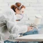 woman spraying paint on a piece of cabinetry using a spray gun