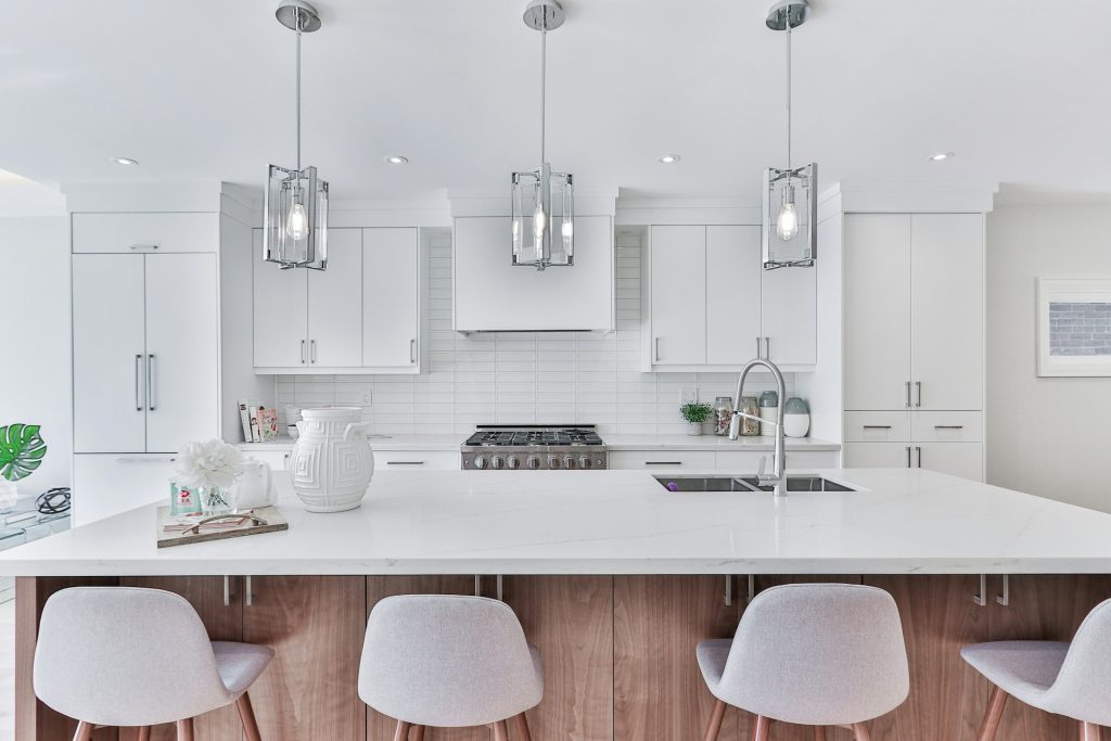 a modern kitchen with stylish white cabinets, an island and 4 stools
